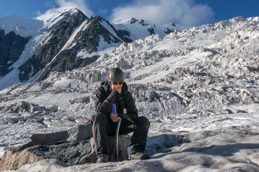 Výšková nemoc. Horolezec dýchá kyslík z nádrže na pozadí ledovce pokrytého sněhem a ledovými horami.
