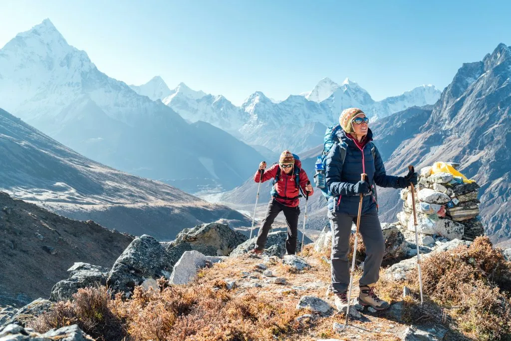 Pár po trekkingové trase Everest Base Camp v okolí Dughla 4620 m. Baťůžkáři s batohy na zádech a trekovými holemi si užívají výhled do údolí s vrcholem Ama Dablam 6812m.